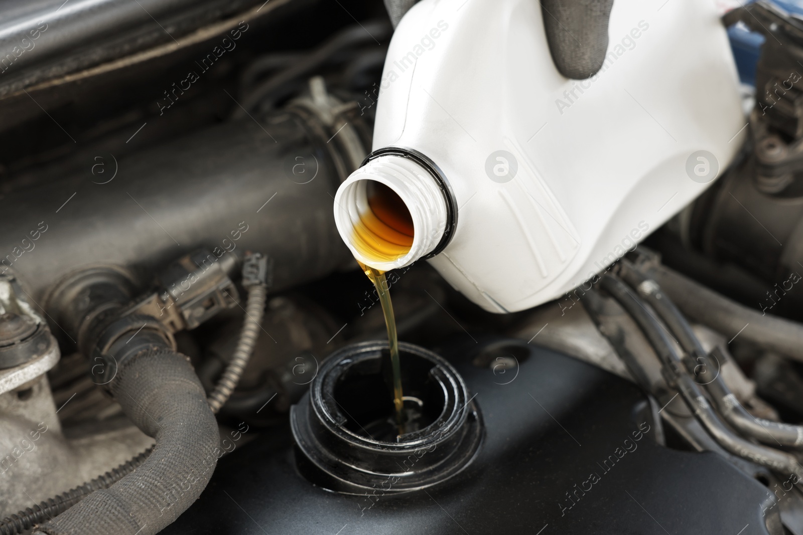 Photo of Man pouring motor oil into car engine, closeup