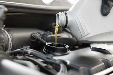 Photo of Man pouring motor oil into car engine, closeup