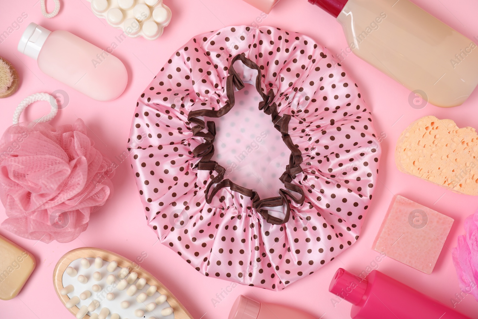 Photo of Shower cap and bath accessories on pink background, flat lay