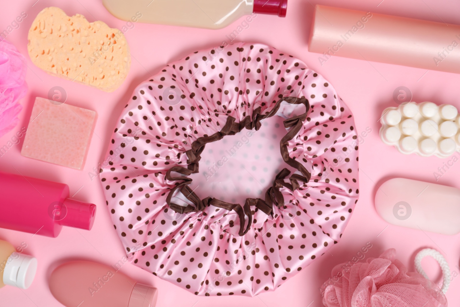 Photo of Shower cap and bath accessories on pink background, flat lay