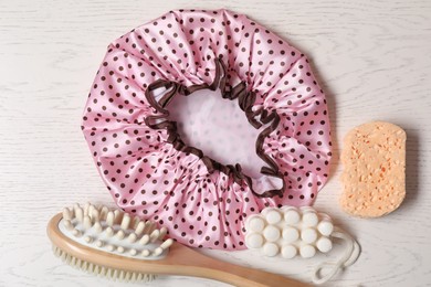 Photo of Shower cap and bath accessories on light wooden background, flat lay