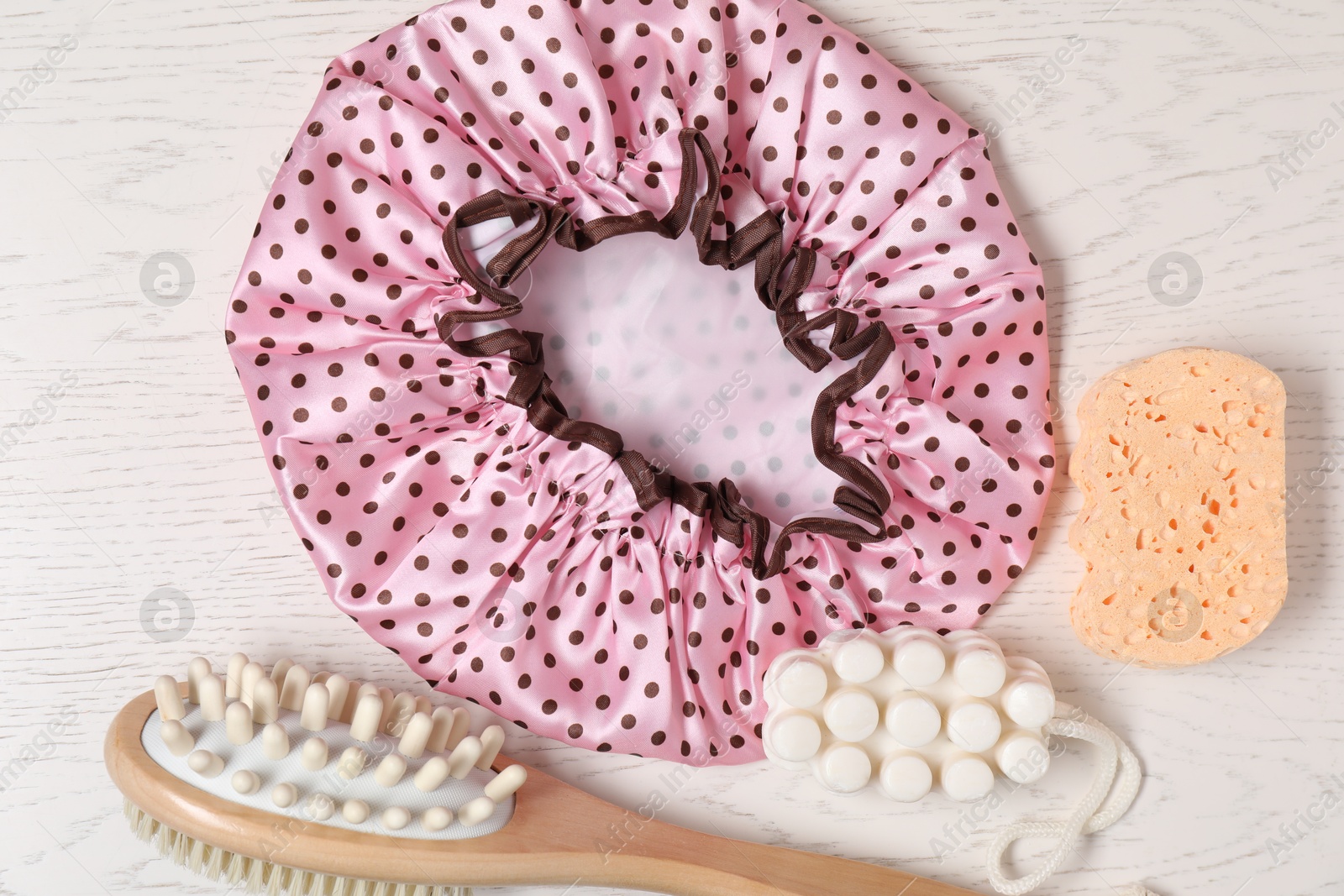 Photo of Shower cap and bath accessories on light wooden background, flat lay