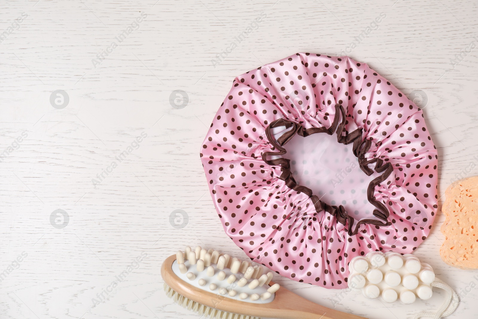 Photo of Shower cap and bath accessories on light wooden background, flat lay. Space for text