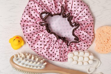 Photo of Shower cap and bath accessories on light wooden background, flat lay