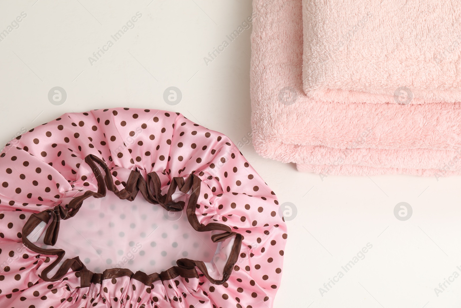 Photo of Shower cap and towels on white table, top view