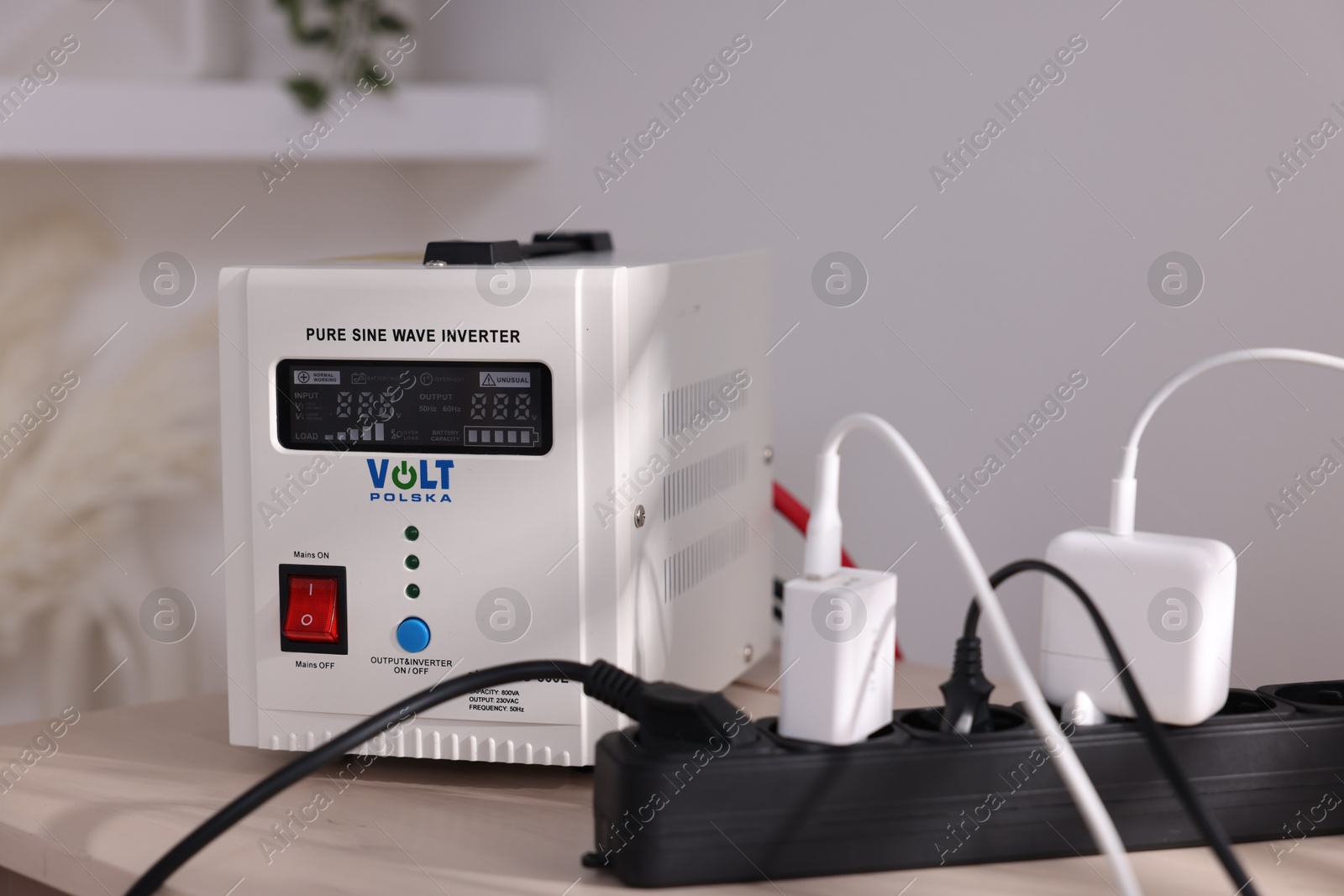 Photo of Portable power station and multi-socket extension board with chargers on table indoors