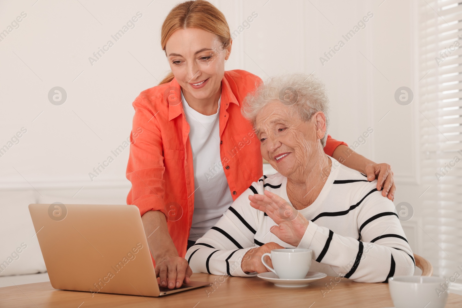 Photo of Caregiver showing something on laptop to senior woman at home