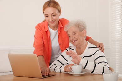 Photo of Caregiver showing something on laptop to senior woman at home