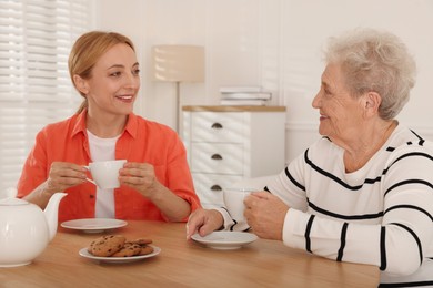 Caregiver and senior woman enjoying hot drink at table indoors