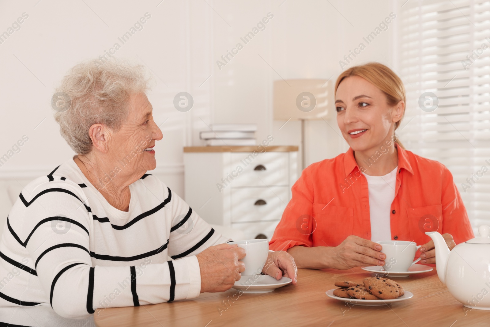 Photo of Caregiver and senior woman enjoying hot drink at table indoors