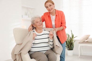 Photo of Caregiver covering senior woman with blanket at home