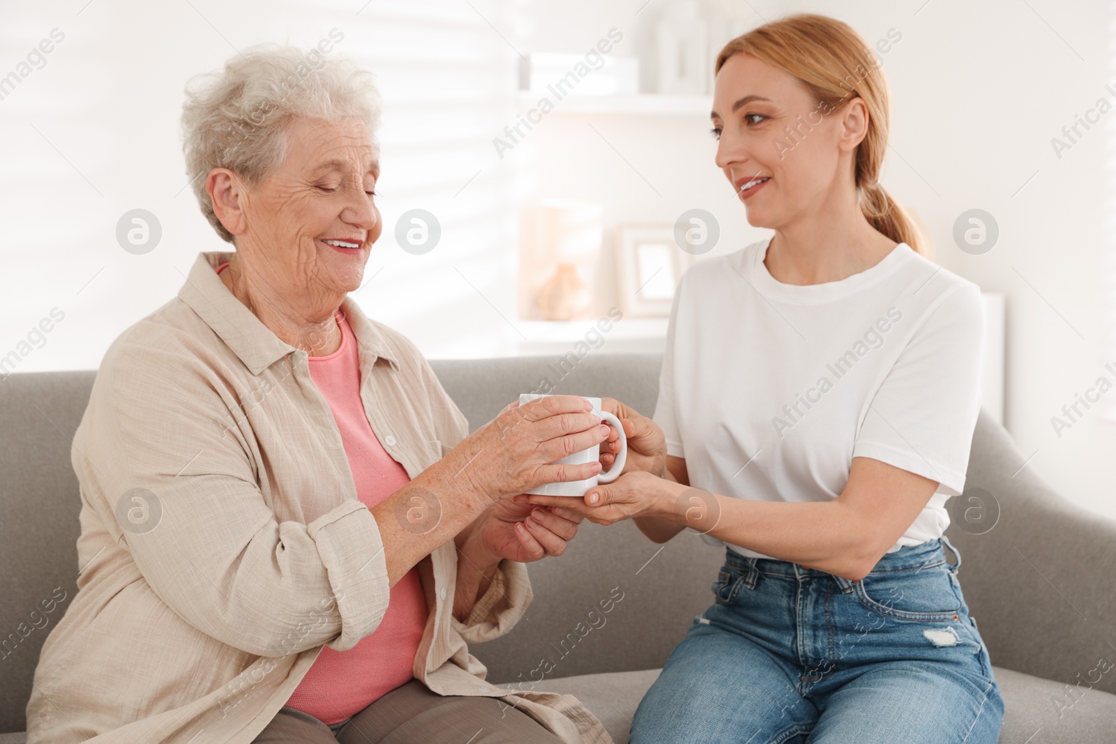 Photo of Caregiver giving cup of drink to senior woman at home