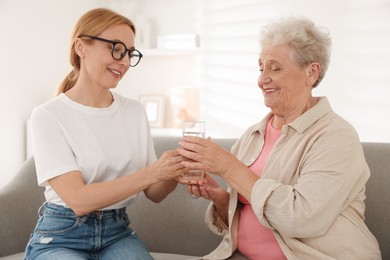 Photo of Caregiver giving glass of water to senior woman at home