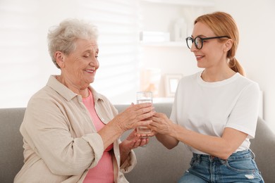 Photo of Caregiver giving glass of water to senior woman at home