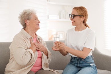 Photo of Caregiver giving glass of water to senior woman at home