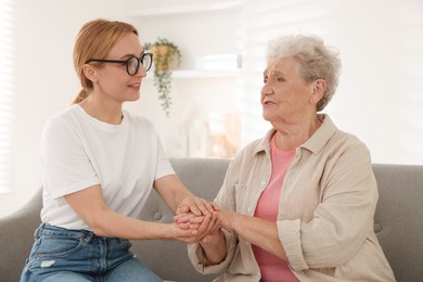 Photo of Caregiver supporting senior woman on sofa at home