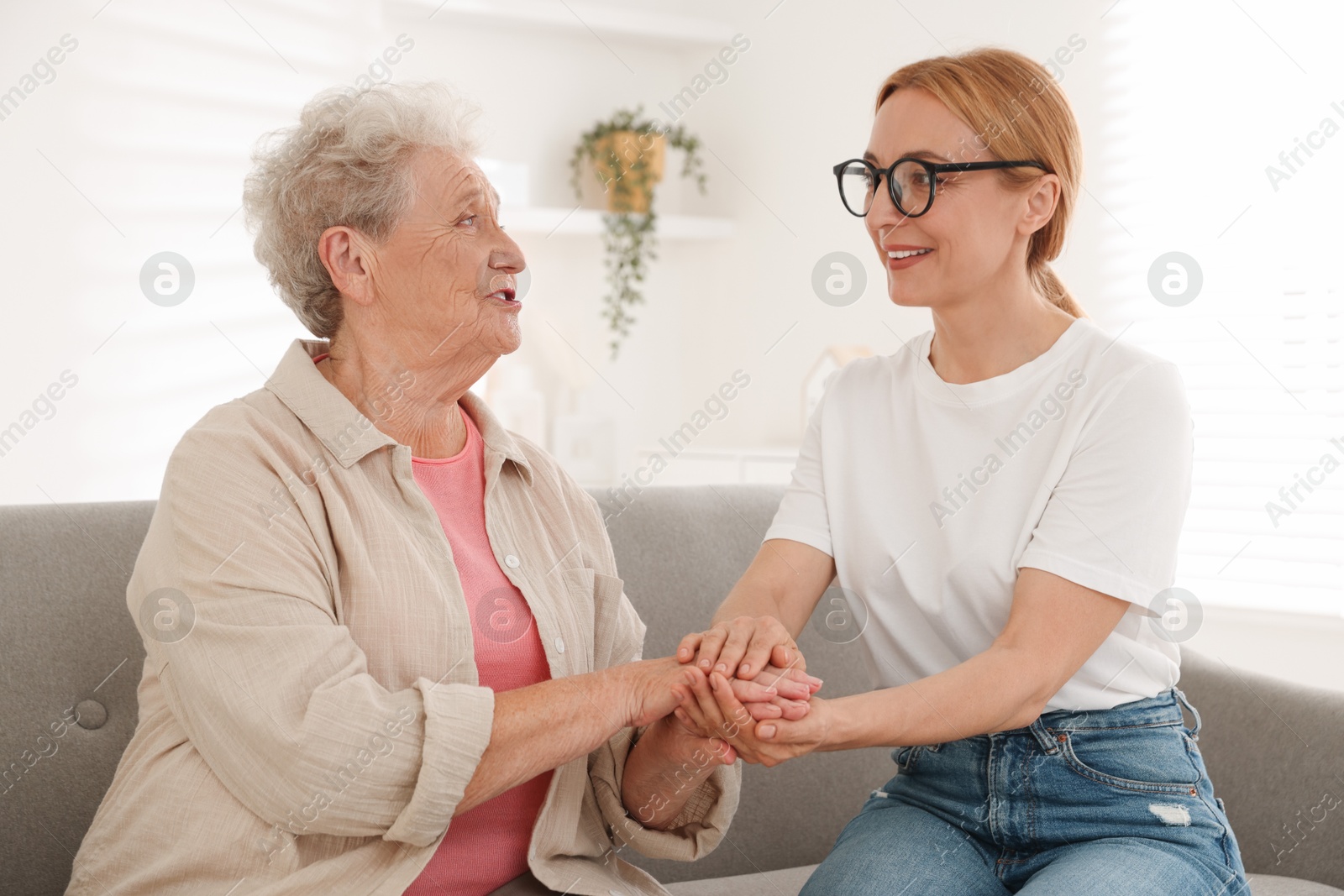 Photo of Caregiver supporting senior woman on sofa at home