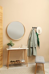 Photo of Coat rack with clothes, mirror and shoe storage benches in hallway. Interior design