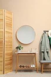 Coat rack with clothes, mirror, shoe storage benches and folding screen in hallway. Interior design