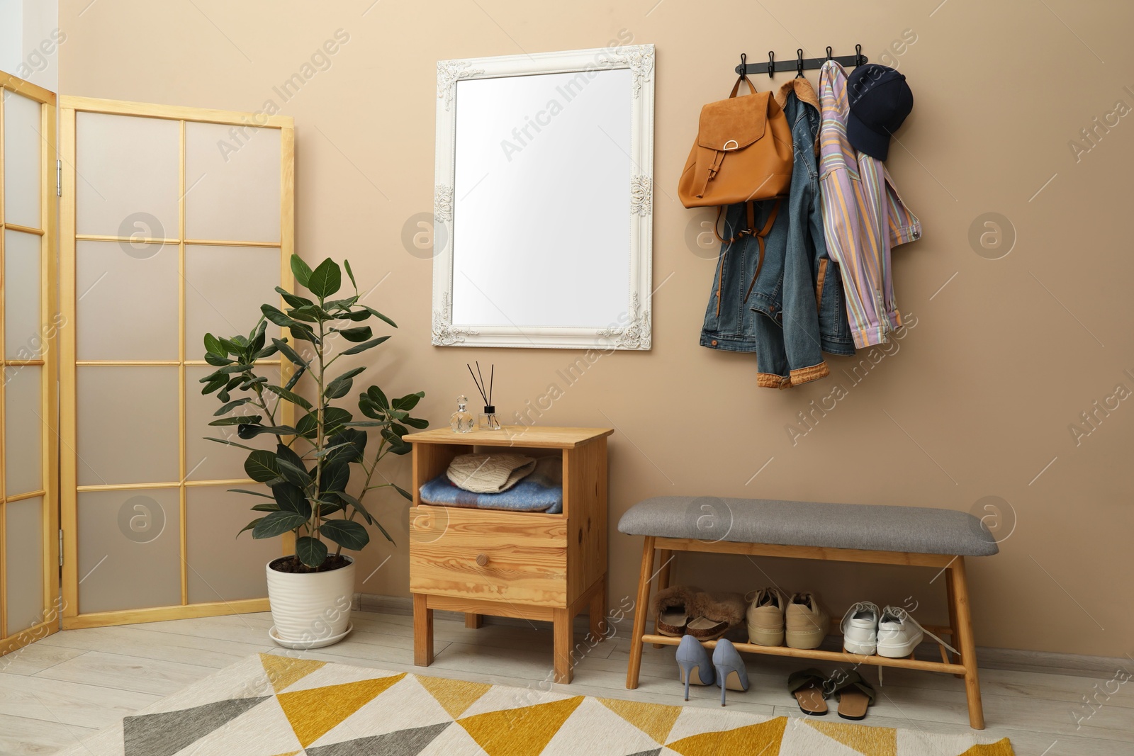 Photo of Coat rack with clothes, mirror, houseplant, shoe storage bench and folding screen in hallway. Interior design