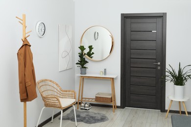 Photo of Clothing rack, mirror, houseplant and stylish furniture in hallway