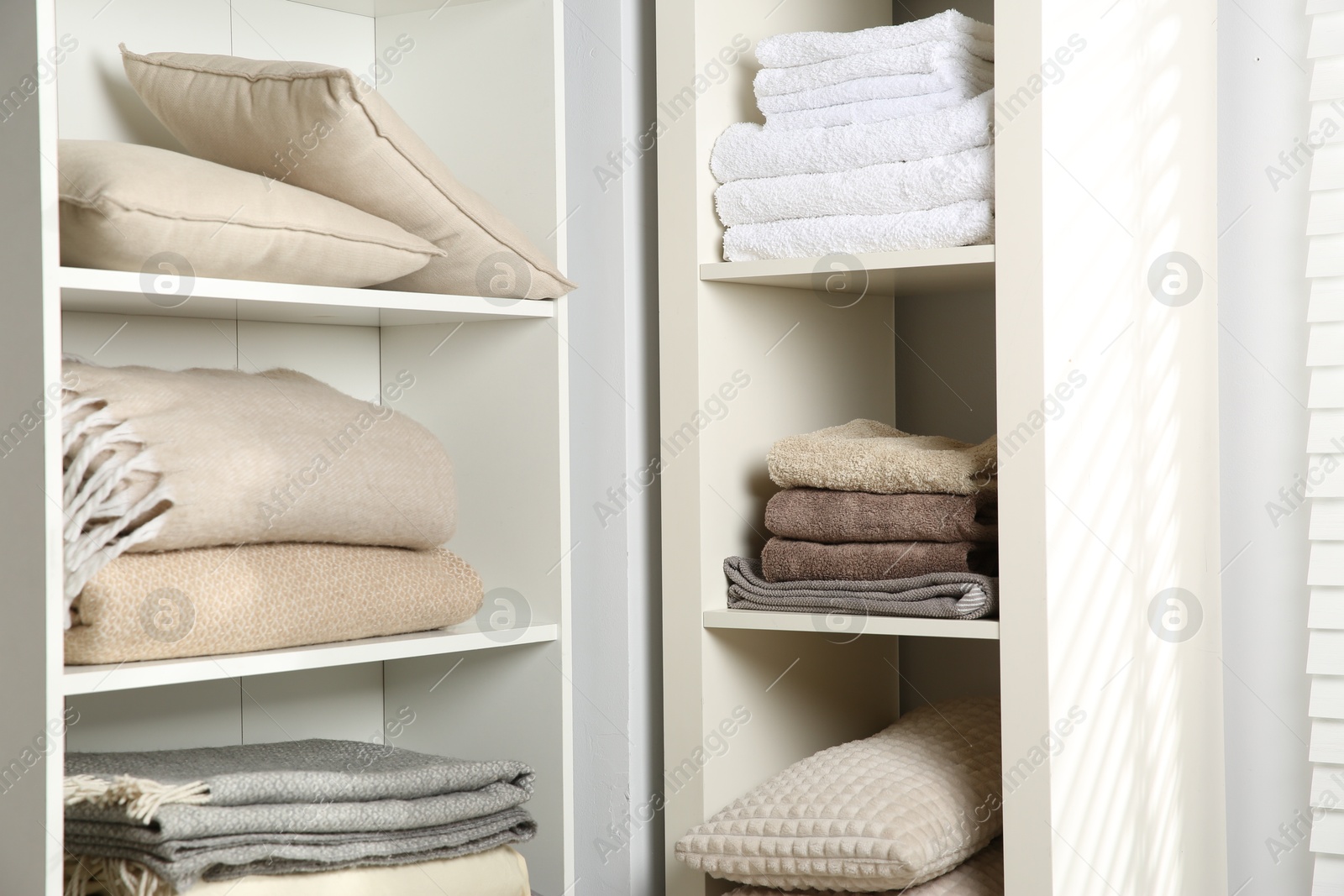 Photo of Home textile organization. Folded towels, blankets and pillows on shelving units indoors, closeup