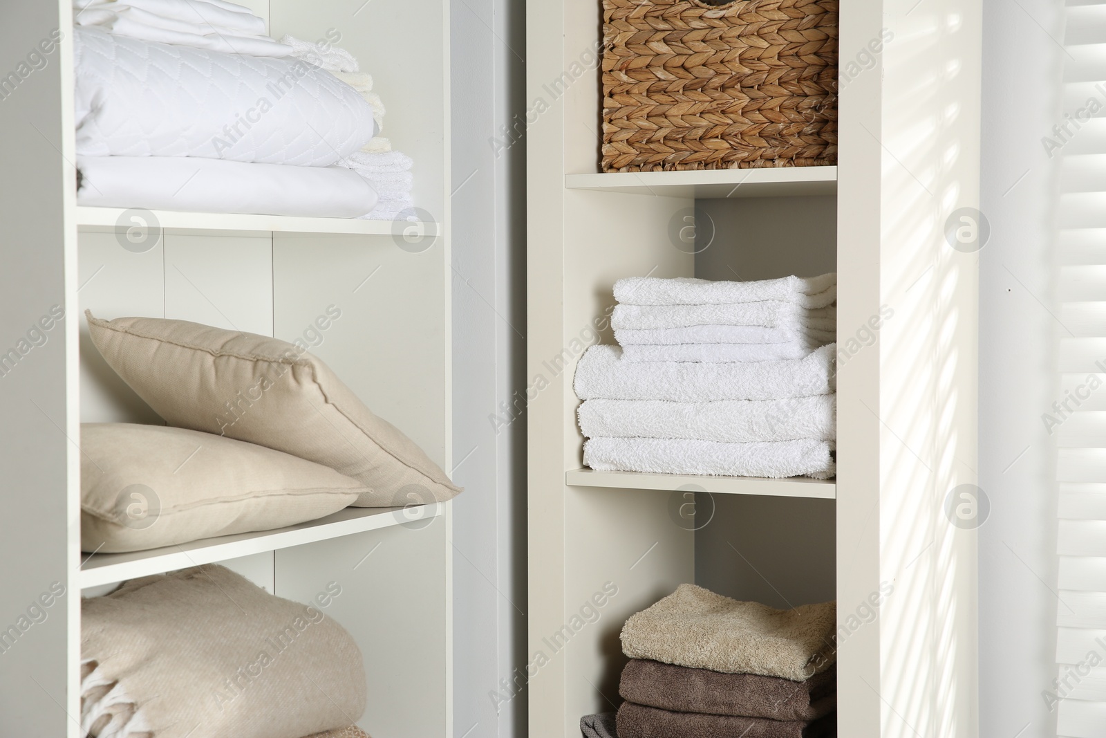 Photo of Home textile organization. Folded towels, blankets and pillows on shelving units indoors, closeup