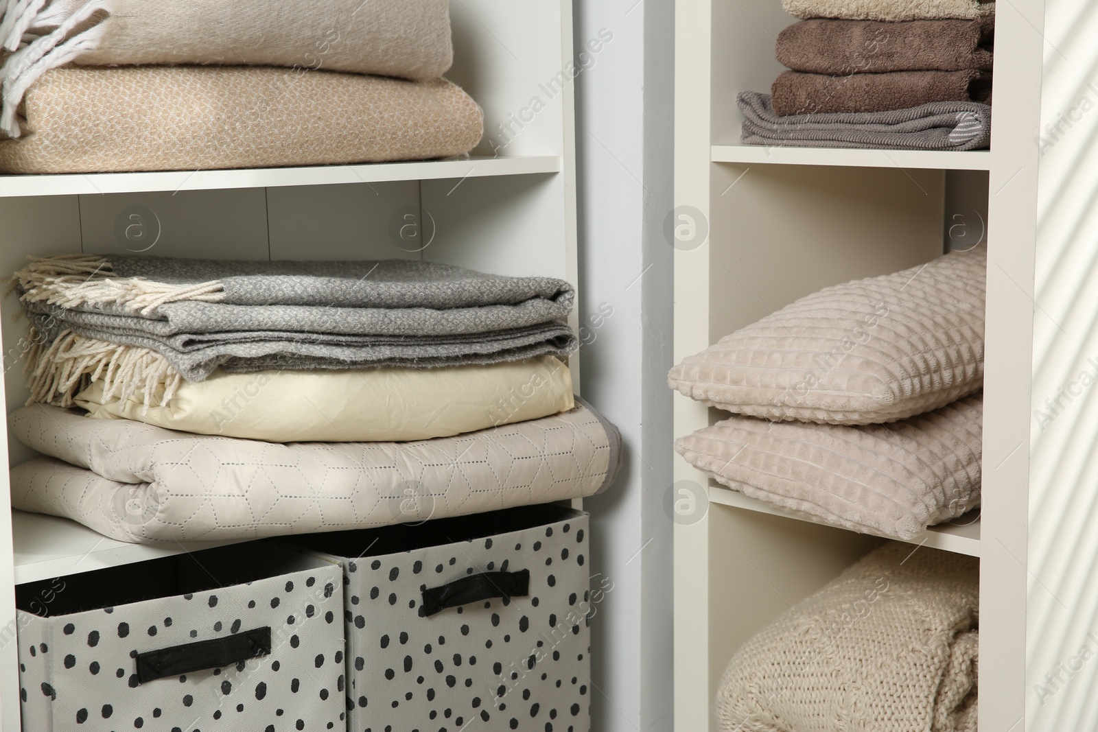 Photo of Home textile organization. Folded towels, blankets and pillows on shelving units indoors, closeup