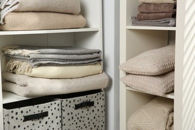 Photo of Home textile organization. Folded towels, blankets and pillows on shelving units indoors, closeup