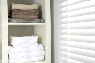 Photo of Home textile organization. Folded towels on shelving unit indoors, closeup