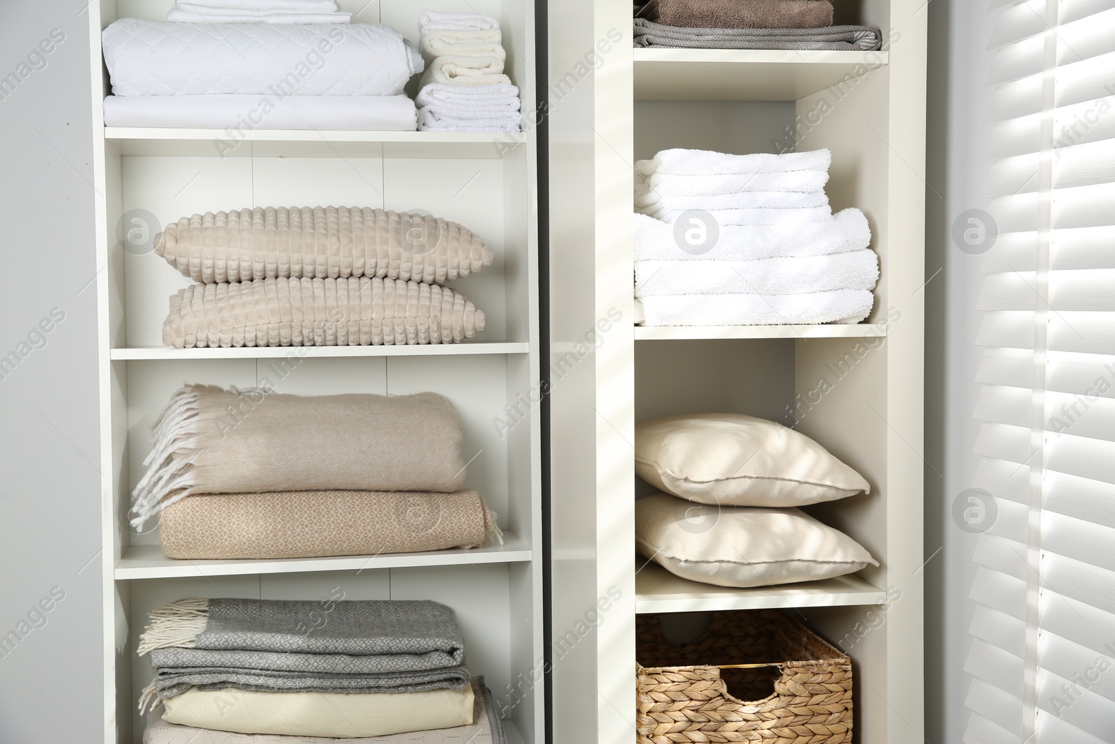 Photo of Home textile organization. Folded towels, blankets and pillows on shelving units indoors, closeup