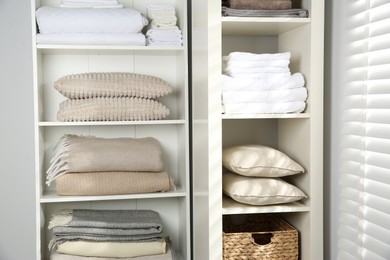 Photo of Home textile organization. Folded towels, blankets and pillows on shelving units indoors, closeup