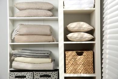 Photo of Home textile organization. Folded towels, blankets and pillows on shelving unit indoors, closeup