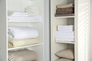 Photo of Home textile organization. Folded towels, blankets and pillows on shelving units indoors, closeup