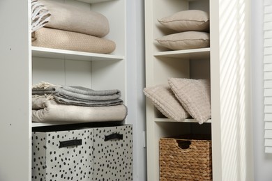 Photo of Home textile organization. Folded blankets and pillows on shelving units indoors, closeup