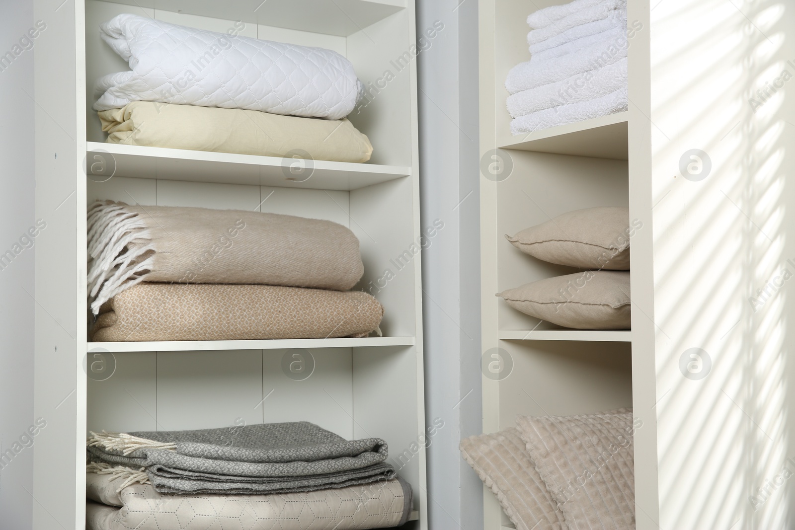 Photo of Home textile organization. Folded towels, blankets and pillows on shelving units indoors, closeup