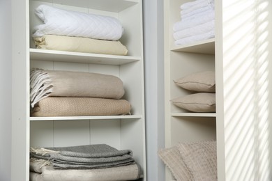 Photo of Home textile organization. Folded towels, blankets and pillows on shelving units indoors, closeup