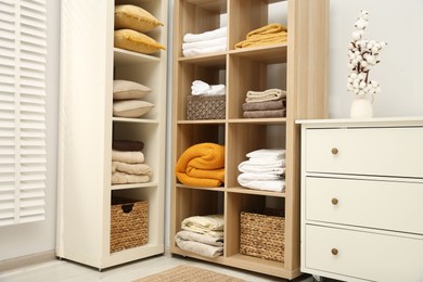 Photo of Home textile organization. Folded towels, blankets and pillows on shelving units indoors