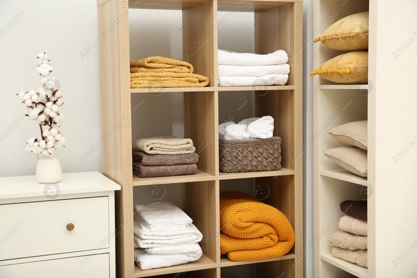 Photo of Home textile organization. Folded towels, blankets and pillows on shelving units indoors