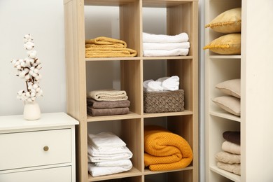 Photo of Home textile organization. Folded towels, blankets and pillows on shelving units indoors