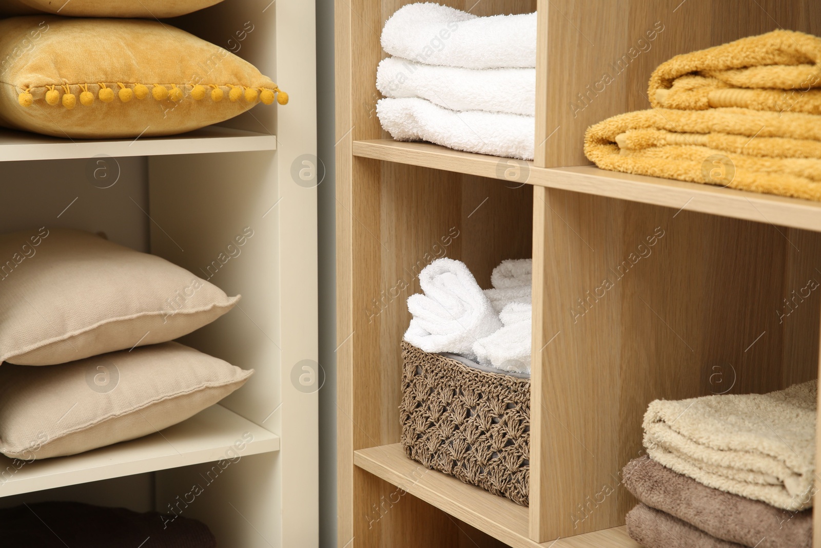 Photo of Home textile organization. Folded towels and pillows on shelving units indoors, closeup