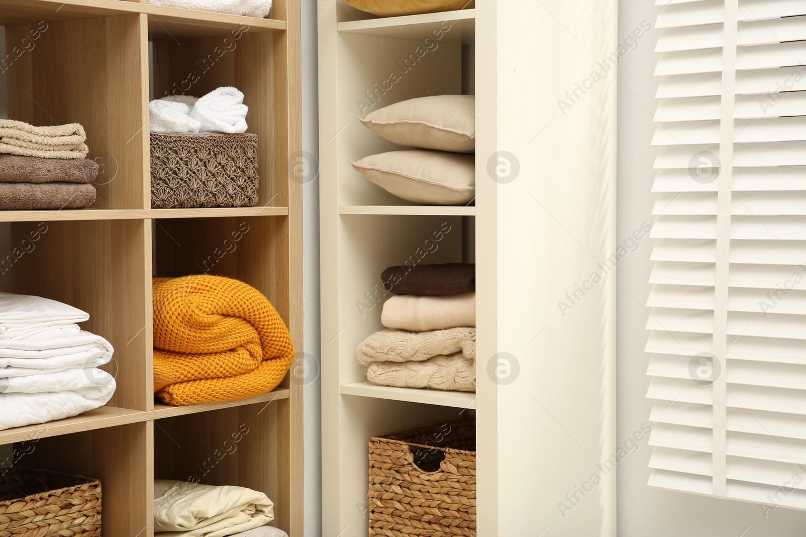 Photo of Home textile organization. Folded towels, blankets and pillows on shelving units indoors