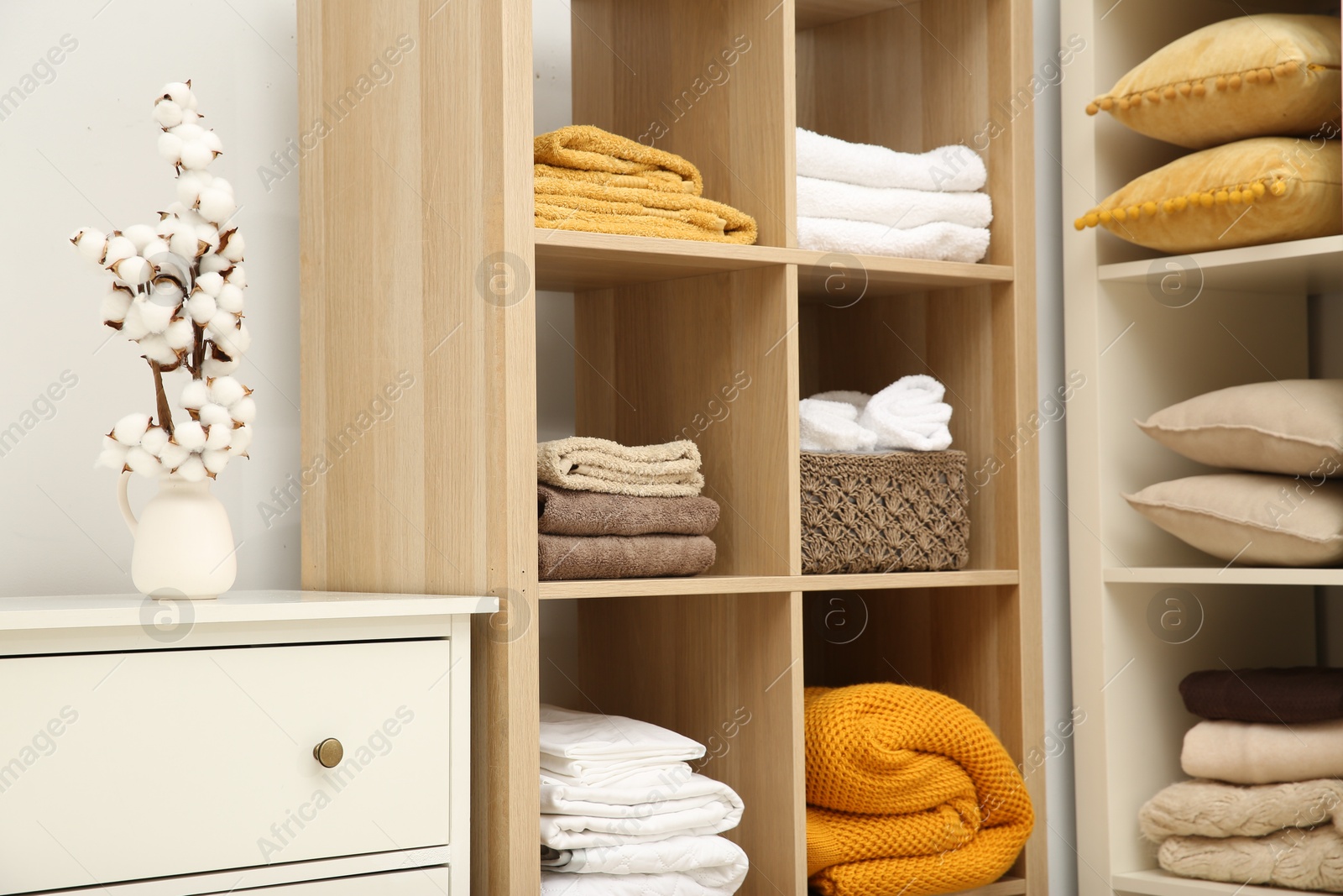 Photo of Home textile organization. Folded towels, blankets and pillows on shelving units indoors