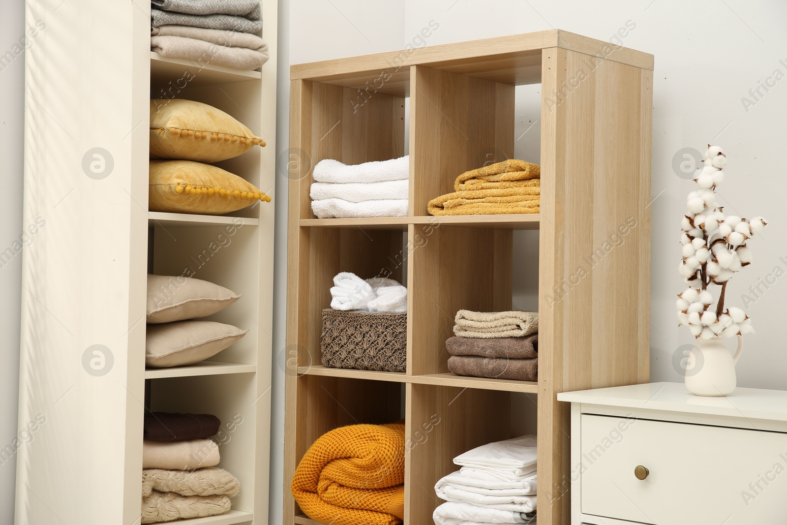 Photo of Home textile organization. Folded towels, blankets and pillows on shelving units indoors