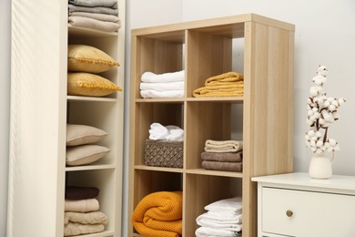 Photo of Home textile organization. Folded towels, blankets and pillows on shelving units indoors