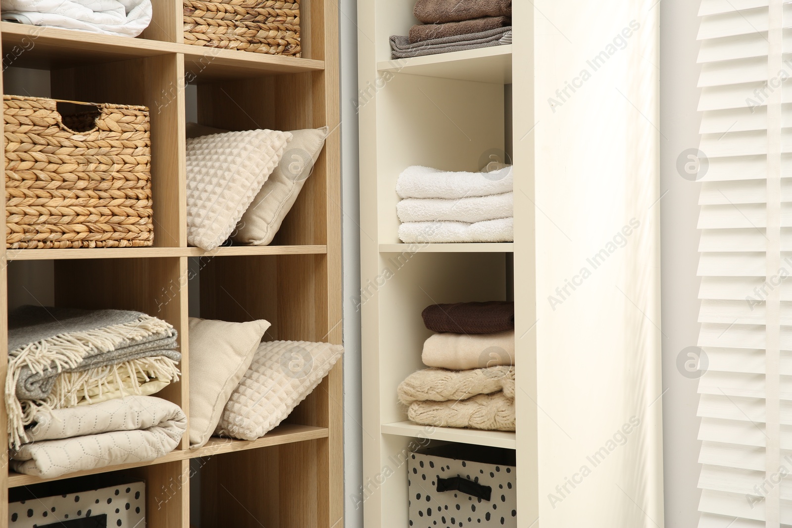 Photo of Home textile organization. Folded towels, blankets and pillows on shelving units indoors, closeup