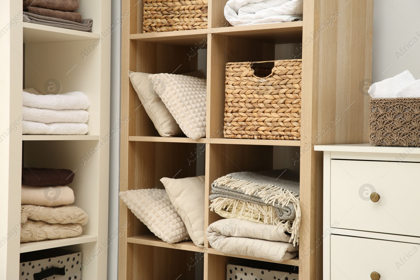 Photo of Home textile organization. Folded towels, blankets and pillows on shelving units indoors, closeup