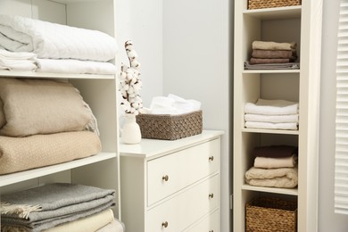 Photo of Home textile organization. Folded towels and blankets on shelving units indoors