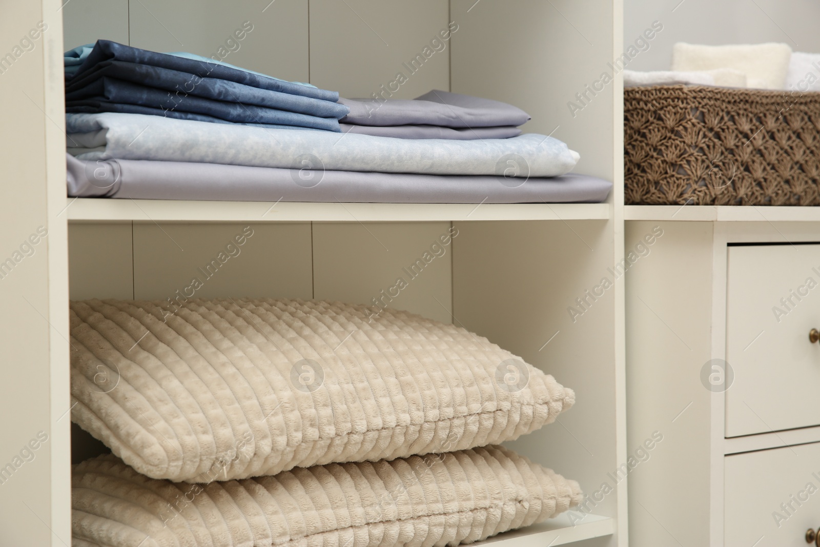 Photo of Home textile organization. Folded bedsheets and pillows on shelving unit indoors, closeup