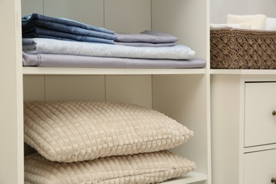 Photo of Home textile organization. Folded bedsheets and pillows on shelving unit indoors, closeup